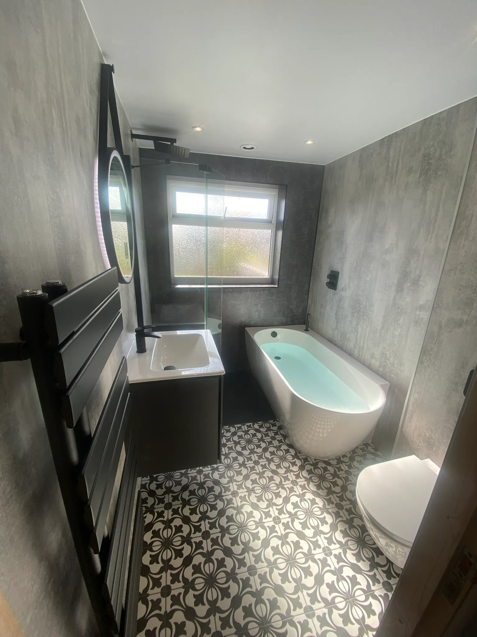 Modern bathroom with grey concrete-effect wall panels, black fixtures and a white freestanding bath.