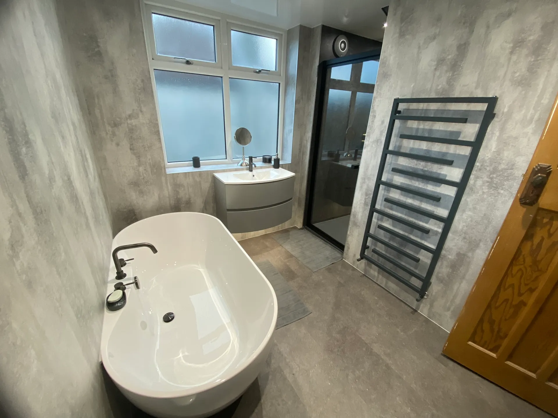 Finished bathroom with a white freestanding bath, a curved wall-hung vanity and a round mirror.