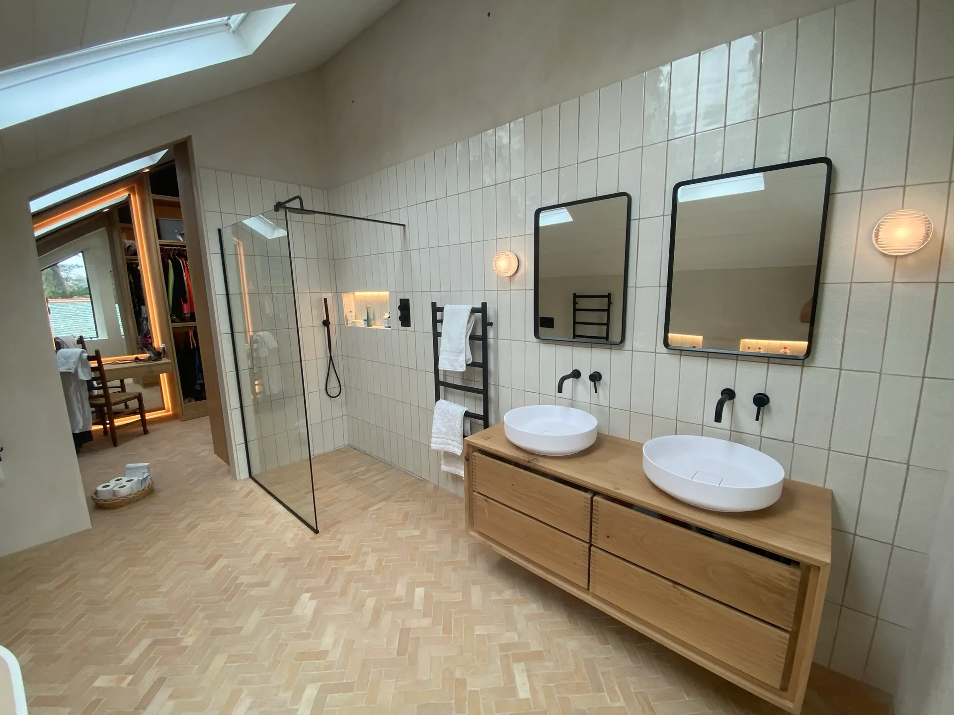 Wide view of the ensuite showing the black-framed walk-in shower, twin-basin oak vanity and herringbone floor.
