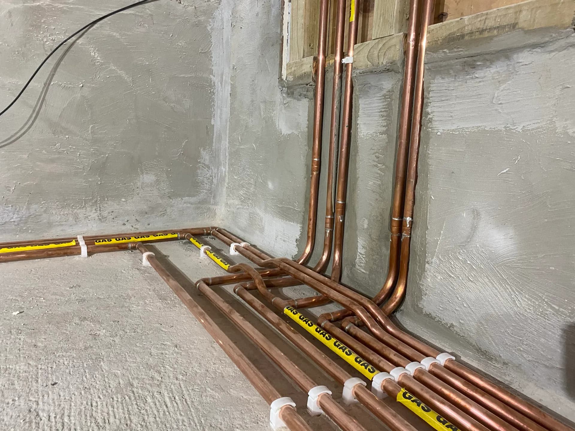 Copper first-fix pipework with vertical risers and floor-level runs, some wrapped in yellow GAS identification tape.