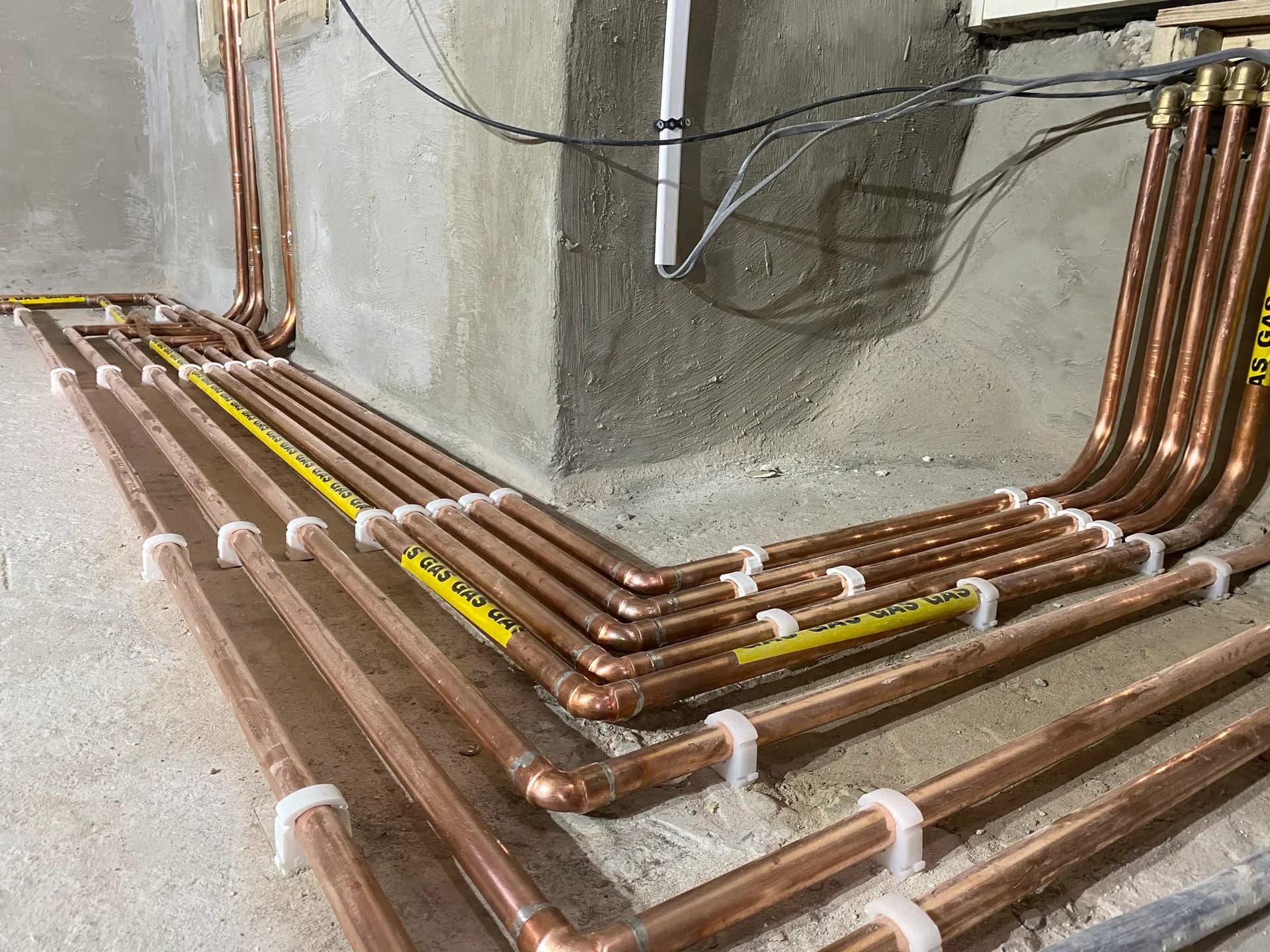 Neatly bent parallel copper gas pipe runs wrapped in yellow GAS identification tape, clipped around a corner.