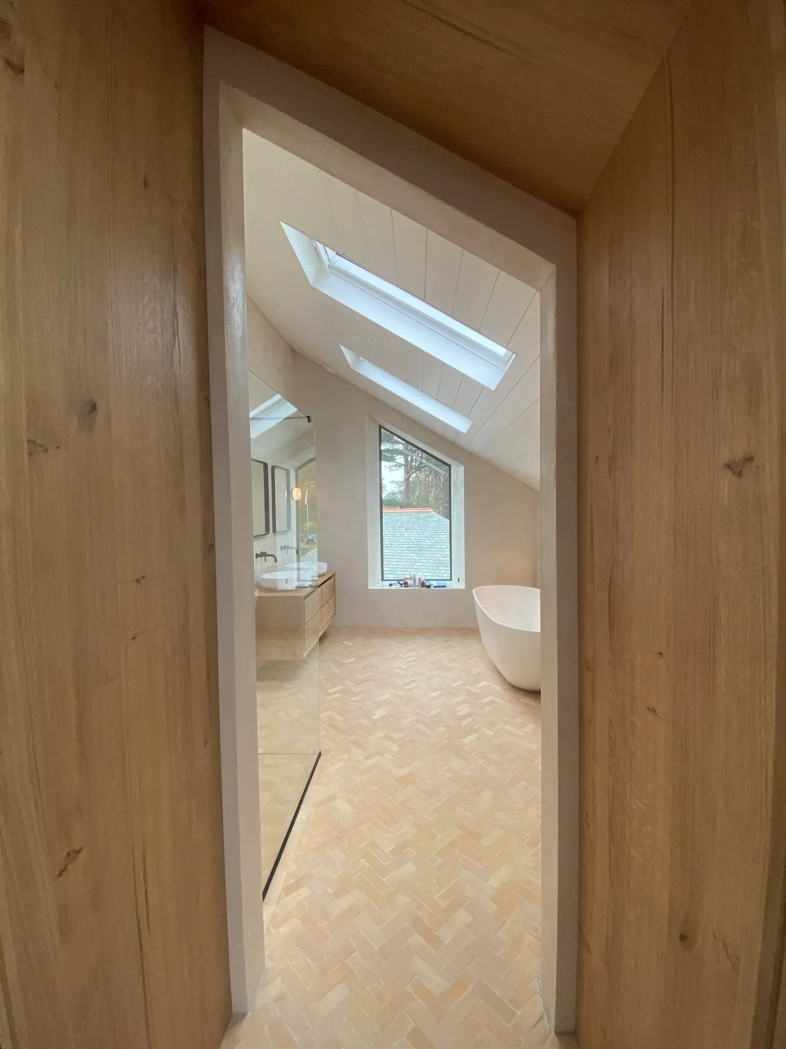 Skylit loft bathroom with a sloped ceiling, freestanding white bath, herringbone floor and a vanity with a vessel basin.