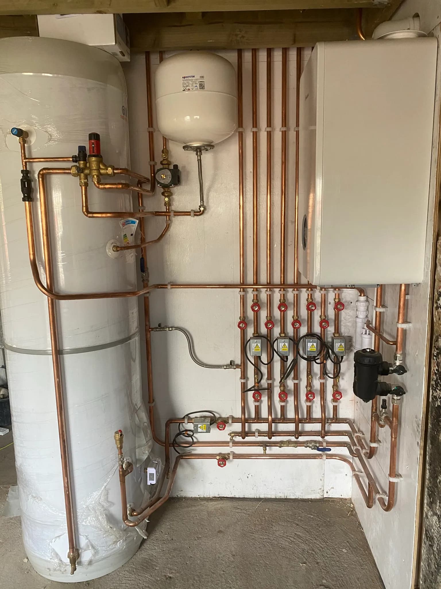 Plant room with a lagged unvented hot water cylinder, a wall-mounted expansion vessel and a circulating pump on copper pipework.