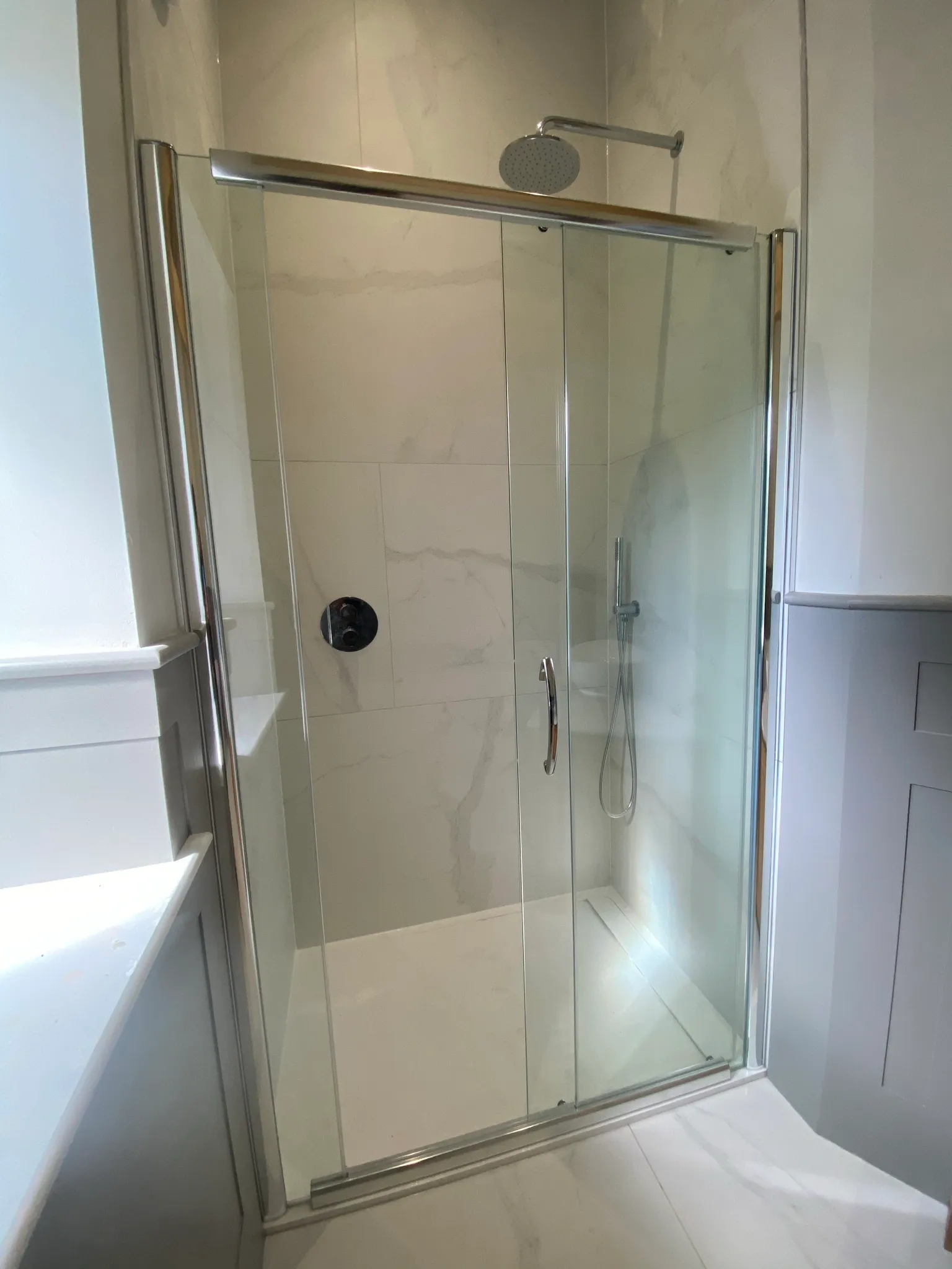 Finished shower enclosure with a chrome-framed sliding glass door, a wall-mounted rainfall head and a handheld shower.