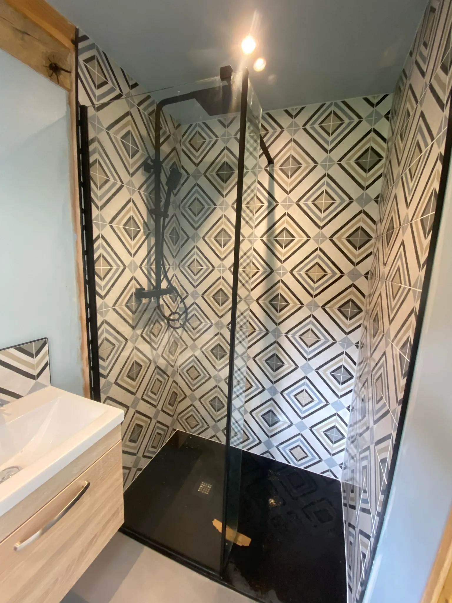 Walk-in shower with bold black, cream and grey geometric diamond-patterned wall tiles and a black riser-rail shower.